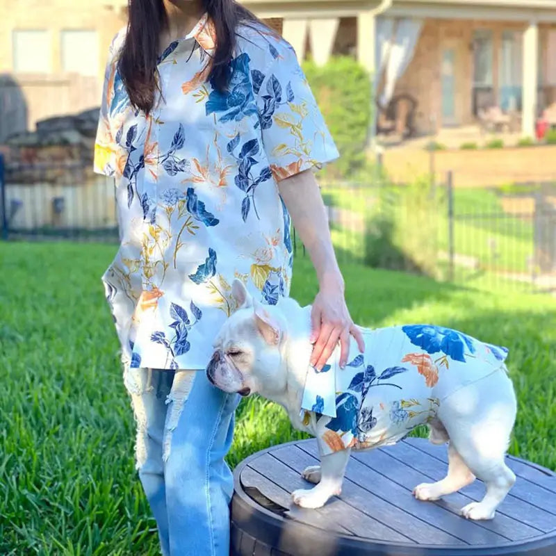 Matching watercolor floral print shirt set for owner and French Bulldog, worn outdoors in a park, with the Frenchie standing beside the owner to show the full outfit design.