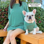 Green and white striped matching outfit for owner and French Bulldog, worn outdoors on a wooden bench.