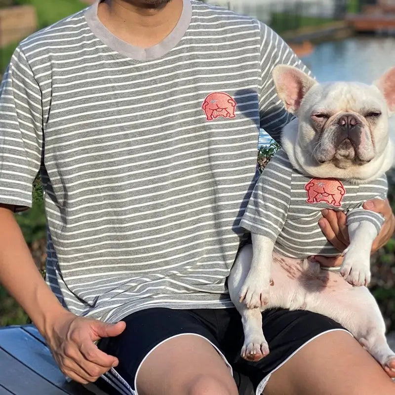 Pet dad holding white French Bulldog in outdoor scenery, both wear matching grey striped pig patch casual family outfit tee