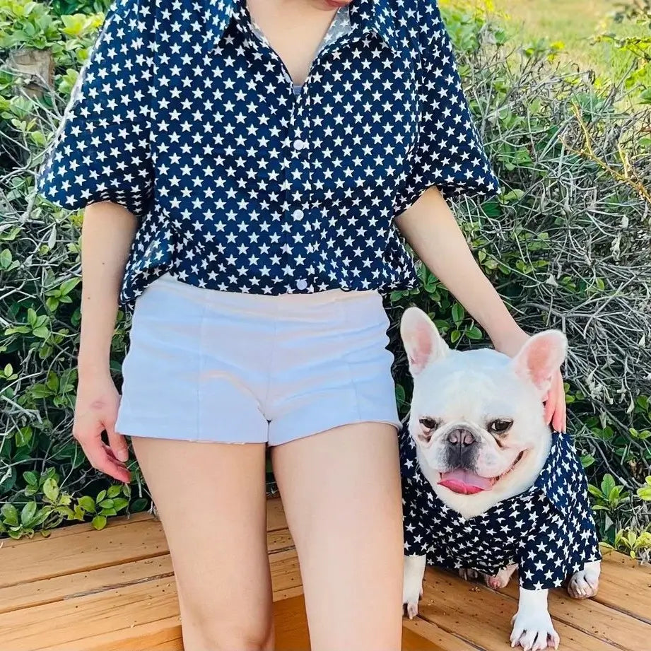 Navy blue star print matching shirt set for owner and French Bulldog, with the owner in a button-up shirt and shorts, and the Frenchie in a matching dog shirt.