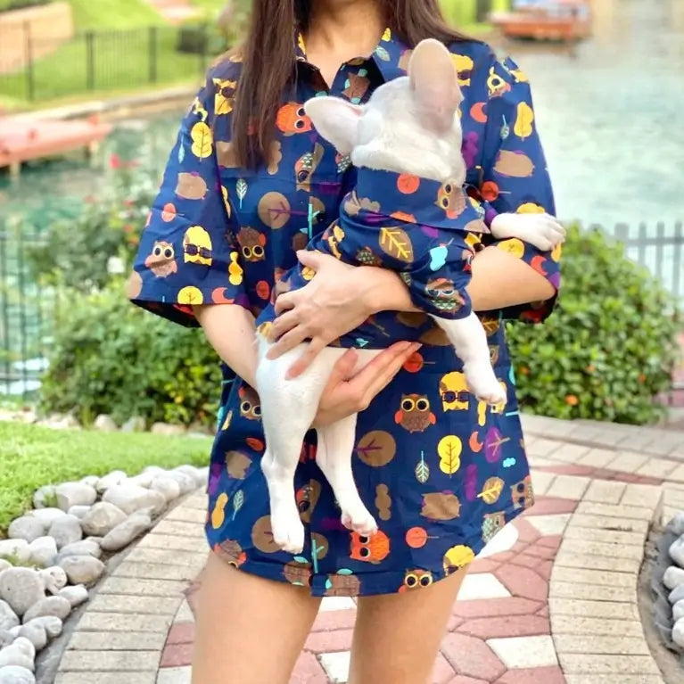 Matching owl print shirt set for owner and French Bulldog, worn outdoors by a lake, with the owner holding the Frenchie in the matching dog shirt.