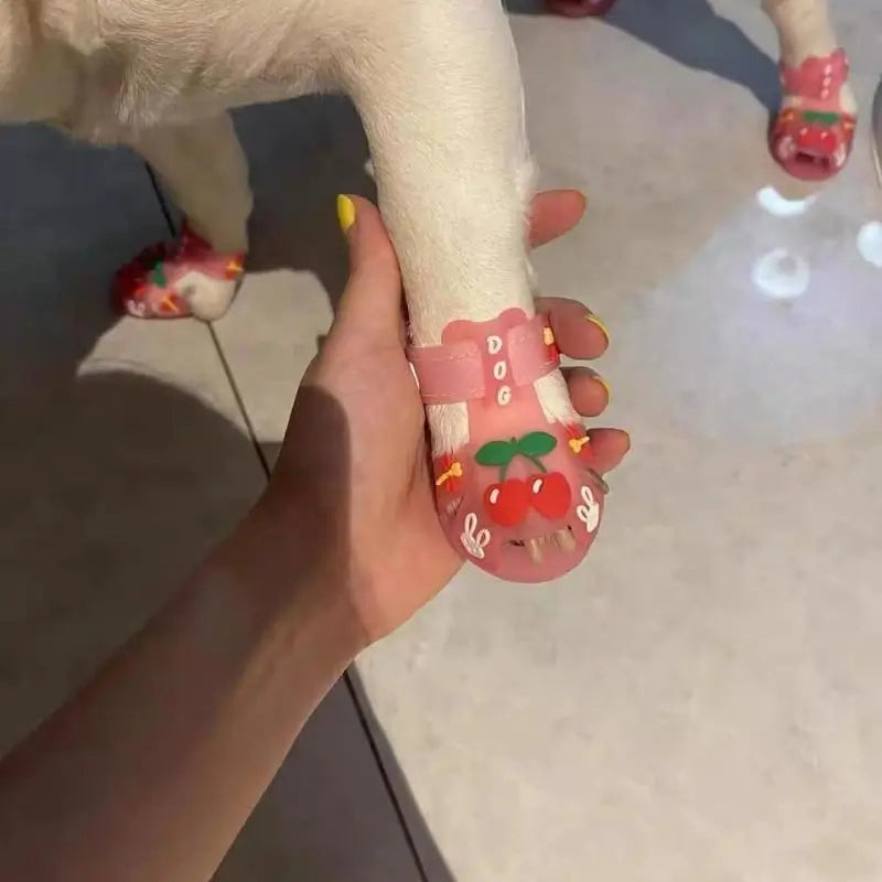 Close-up view of pink pet sandals with cherry and rabbit designs on a French Bulldog paw, showing adjustable strap and cute details.