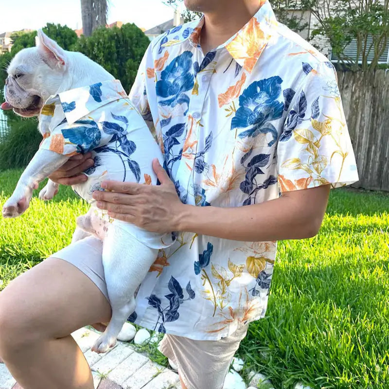 Matching watercolor floral print shirt set for male owner and French Bulldog, worn outdoors on a grassy lawn, highlighting the pet shirt fit and family matching style.
